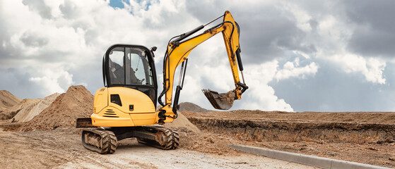 A mini excavator digs the earth, shaping the landscape at a busy construction site. Using compact equipment for construction work © Anoo