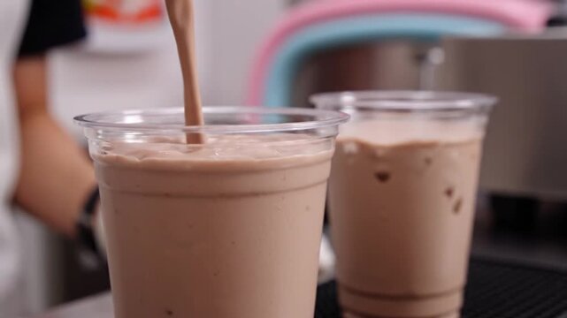 Capturing the smooth pour of a delicious chocolate milkshake into a clear plastic cup, highlighting the creamy texture and rich color, ready for a refreshing treat in a vibrant setting