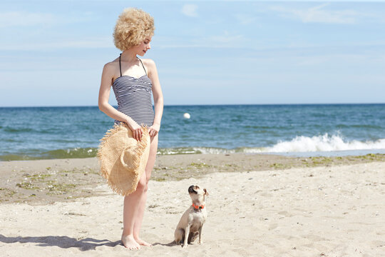 Young woman in swimsuit with straw hat and dog on the beach