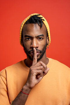 Portrait of stylish young man shushing in front of orange wall