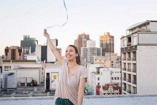 Young woman standing on a rooftop terrace, playing with a ribbon