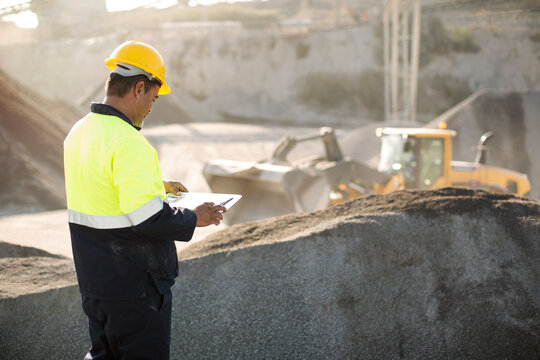 Worker standing at quarry, using clipboard