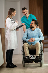 Obraz premium Doctor consulting patient in wheelchair with nurse assisting