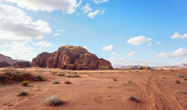 Wadi Rum red orange desert with small rocky hills, vehicle tire print visible in sand