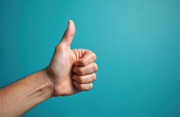 Hand shows thumb up gesture on turquoise background. Symbolizes approval good job success agreement. A person expresses positive feedback acceptance and liking for something.