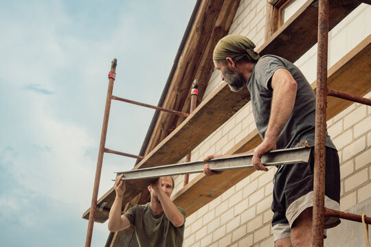 Two professional builders working on scaffolding at a residential construction site under a clear sky