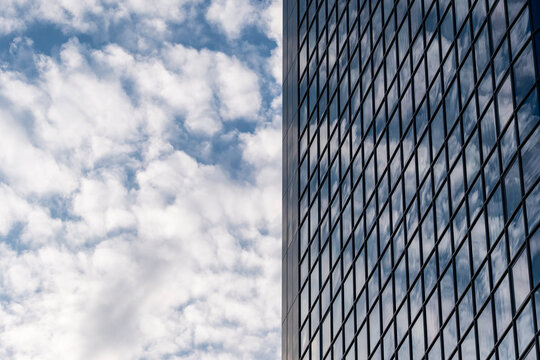 Modern urban building facade with windows pattern and dramatic perspective reaching into sky with clouds creating a clean background for corporate copy space design