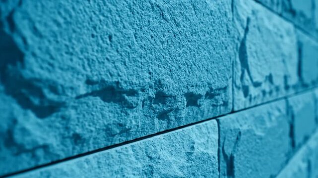 Close-up of cyan-colored brick wall, showing textured surface with light and shadows creating depth