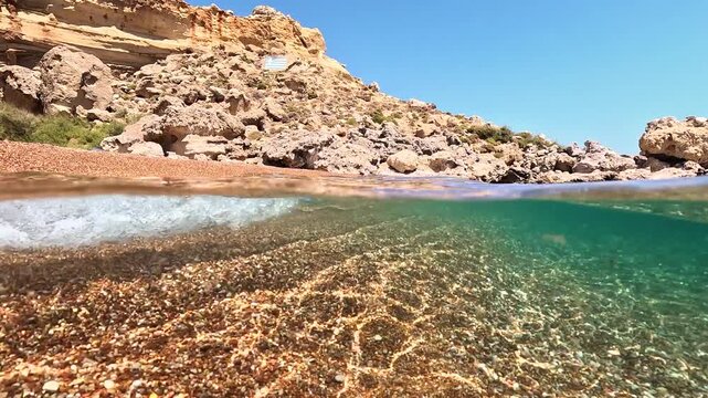 Red sand beach on Rhodes island, Greece. Split underwater video, shallow water with distinctive color shore ground, rocky cliffs in background