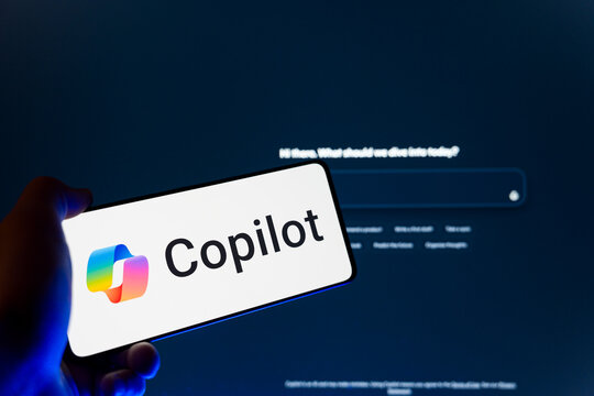 Hand holding smartphone displaying Microsoft Copilot logo on screen with blurred website background, generative artificial intelligence and digital virtual assistant concept