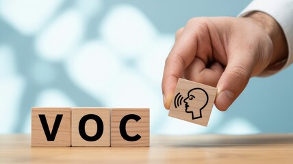 Conceptual image of a hand placing a wooden block with a speaking icon alongside VOC letters on a light table