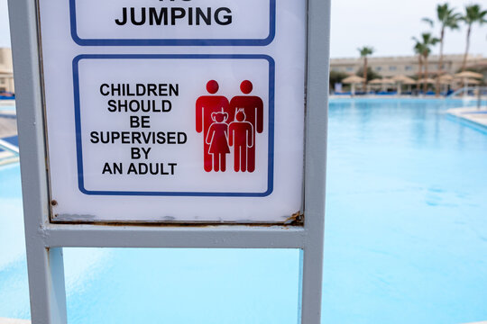 Pool safety sign indicating no jumping and supervision requirements for children near a swimming pool with clear blue water in the background