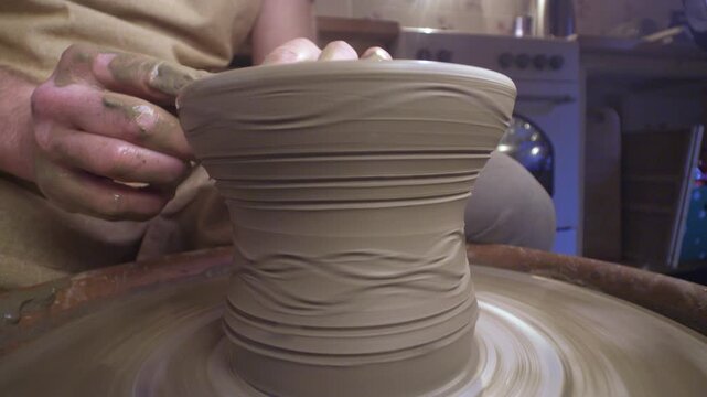 A craftsperson shapes a clay pot with intricate wave patterns on a pottery wheel, highlighting artistry and precision in a traditional workshop.