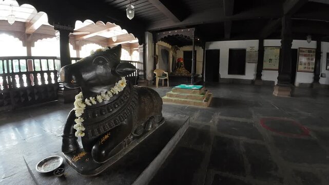 Majestic black stone Nandi bull statue adorned with flowers inside the historic Rajwada Palace temple featuring traditional wooden architecture.