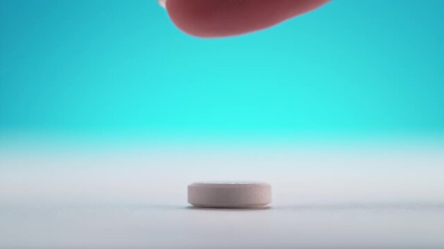 Giving Aspirin For A Headache, The Pill Is Slid Across The White Table With A Finger in Macro and Slow Motion on the Blue Background