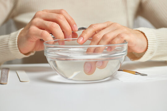 Woman hands soaking fingernails in a bowl of water during a beauty routine