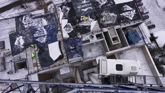 Aerial drone shot of an active construction site during winter with snow-covered surfaces. Overhead view capturing urban development and building process in cold weather.
