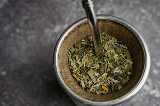 Close up of dried yerba mate leaves in a palo santo matero with bombilla. Natural herbal infusion on dark textured background, traditional South American drink and healthy lifestyle concept.
