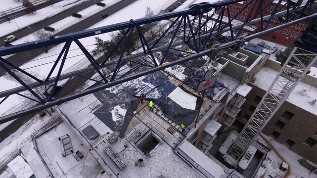 Aerial drone shot of an active construction site during winter with snow-covered surfaces. Overhead view capturing urban development and building process in cold weather.
