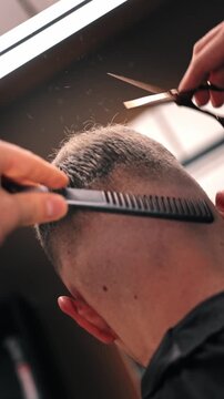Cinematic close up of hair particles flying while barber cuts fade haircut. Warm light atmosphere in modern barbershop. Male grooming concept, stylish haircut process. Vertical 4K.