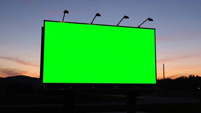Large green billboard with four streetlights against a serene sunset or sunrise sky with silhouette of trees and hills.