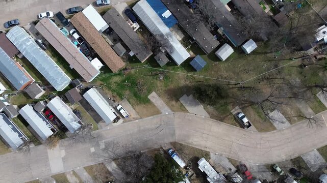 Parallel mobile home rows sit inside trailer park near US 75 and E Parker Rd, tight spacing and consistent lot orientation. Faded shingles, dormant trees, neutral siding tones in Plano, Texas