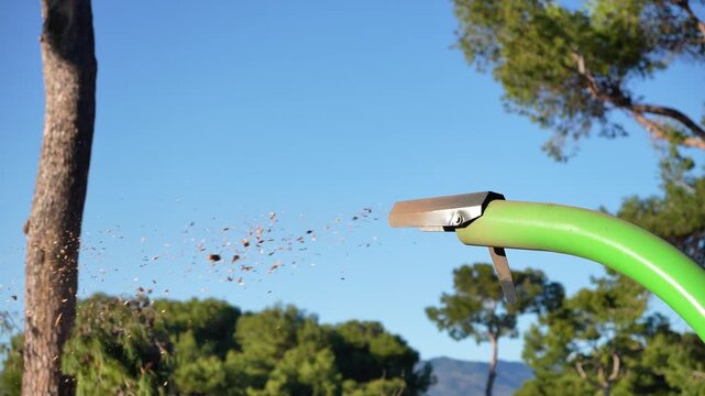 A green and silver branch shredder machine with a green hose coming out of it. The hose is spewing out a lot of dirt and debris