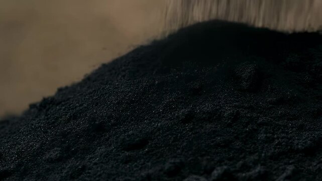Close-up of black powder being poured, showcasing its texture and fine particles. Ideal for industrial applications and material science exploration