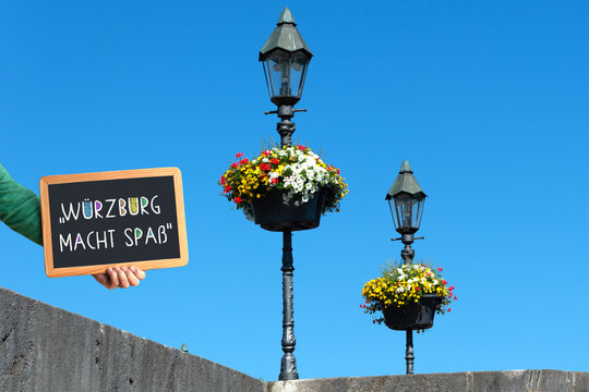 Blumenampeln mit einem Marketingspruch &bdquo;W&uuml;rzburg macht Spa&szlig;&ldquo; auf der Alten Mainbr&uuml;cke in der Stadt W&uuml;rzburg