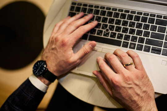 Man&rsquo;s hands typing on laptop keyboard, wearing black watch and gold wedding ring, professional remote work setting