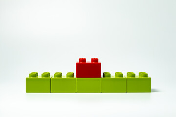 Green plastic building blocks arranged in a horizontal row with one red block standing above the others on white background. Concept of leadership, individuality and standing out from the crowd.