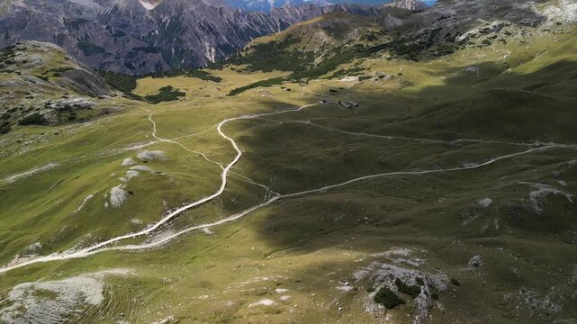 Aerial drone footage over Sennes highlands Dolomites Italy, begins on mountain skyline then tilts down to switchback footpaths across limestone turf and scattered stones