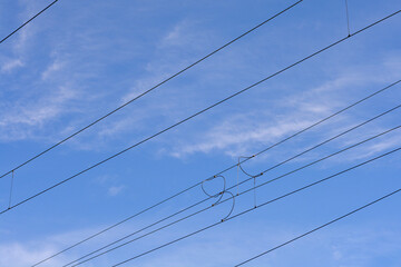 Multiple black electrical power lines stretch diagonally across a clear blue sky with light wispy clouds