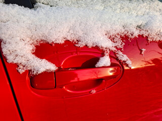 Snow clings to the side window and door handle of the red car
