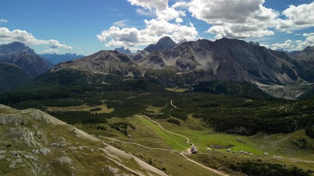 High altitude drone view of karst trail on Sennes Plateau in the Dolomites, rocky slopes and winding path lead to peaks under drifting clouds in South Tyrol Italy