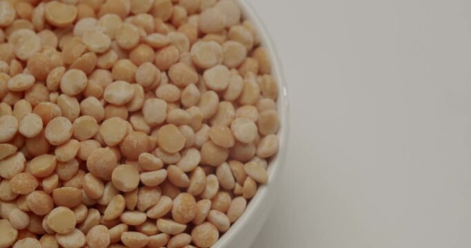 Dry yellow split peas slowly falling into a full white ceramic bowl in a studio setting isolated on a white background, Dry yellow split peas in a white ceramic bowl rotating on a white background