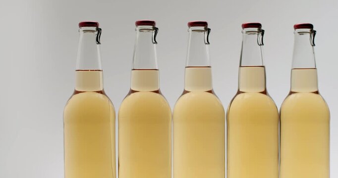 Group of refreshing cider bottles with swing top caps slowly rotating on a clean, Clear glass bottles filled with fresh, unfiltered apple cider isolated on a white background.