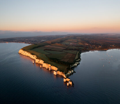 Aerial view of Old Harry Rocks standing defiant against the relentless sea, framed by the golden hues of the sunset, Swanage, England, United Kingdom.