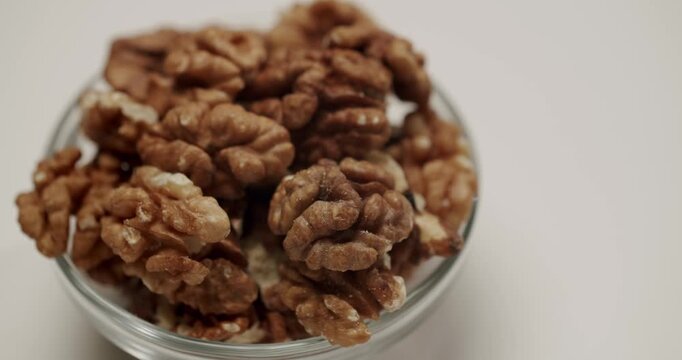 Macro shot of delicious and organic nut kernels, a healthy superfood snack rich in vitamins and minerals. Peeled walnuts in a transparent glass bowl rotating in slow motion,