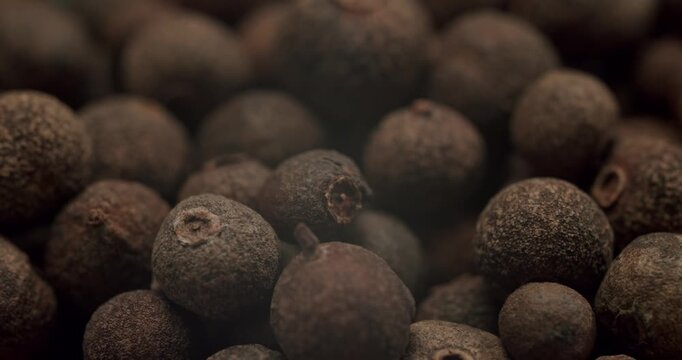 Aromatic allspice berries falling in a rotating pile, creating a dynamic textured background. This extreme close-up in slow motion reveals the detailed surface of the Jamaica pepper spice.