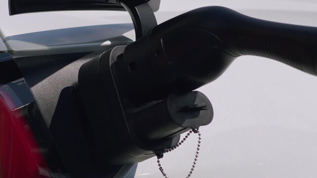 Close-up shot of an electric vehicle charging port with charging connector being plugged in. Modern white electric car at charging station. Sustainable transportation, green energy, zero emissions. 