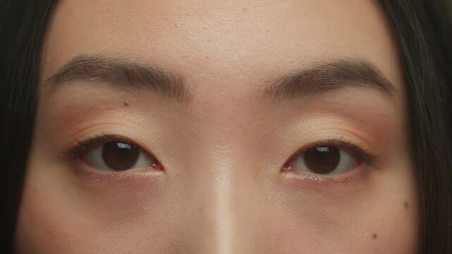 Close up Asian ethnic woman female black eyes looking at camera blinking natural beautiful face Korean Japanese Chinese girl eyesight vision laser correction medicine blink long eyelashes health care