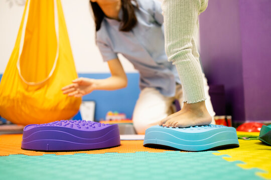 Child receiving pediatric physical therapy for balance and coordination, performing rehabilitation exercises on sensory stepping stones with a therapist assisting