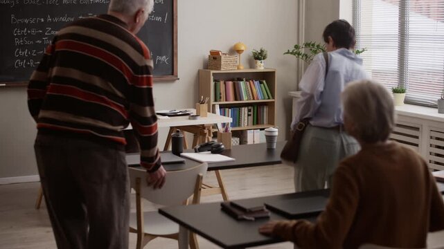 Smiling Black female teacher greeting senior students in bright contemporary classroom with chalkboard and desks during beginning of academic lesson