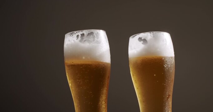 Two frosty glasses filled with golden pilsner beer and frothy foam clinking together in a celebratory toast, splashing golden liquid against a dark background in super slow motion