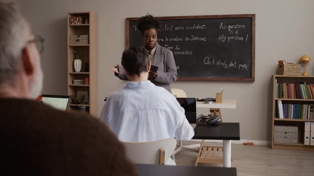 Senior student actively raising hand while Black female teacher guiding interactive discussion and learning in classroom environment