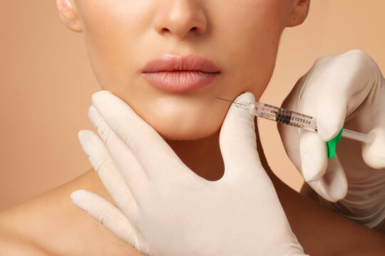 Woman receiving beauty injections with fillers for chin shape correction, beautician holding syringe near woman's chin, procedure chin contouring