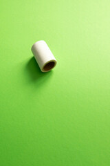Obraz premium A white medical tape roll sits on a vibrant green surface with ample negative space. A minimalist composition focusing on medical supplies and first aid care. vertical