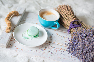 wooden vintage tray with a cup of cappuccino and a macaron on a white bedspread. top view composition. cozy warm home atmosphere, soft morning light and relaxed lifestyle concept.
