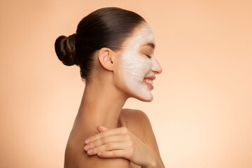 Fresh skin renewal. Profile shot of young lady with face mask posing over beige background, enjoying spa treatments, side view © Home-stock